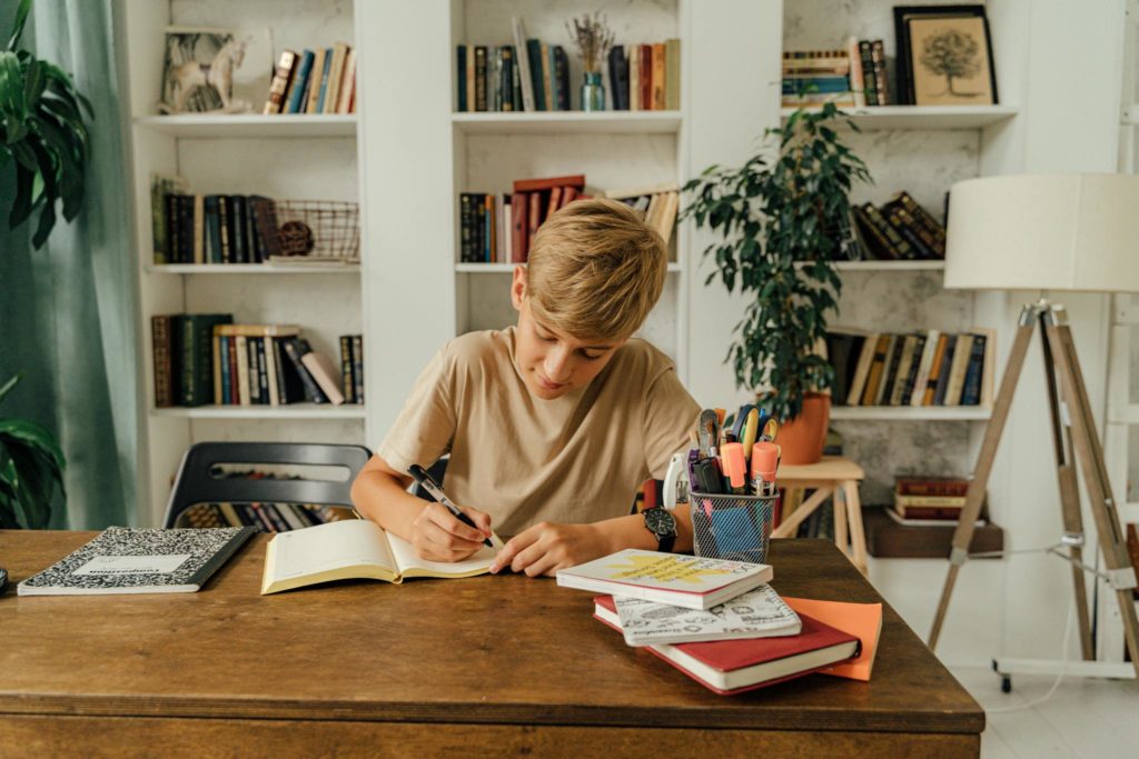 Boy in Brown Shirt Writing on Notebook 