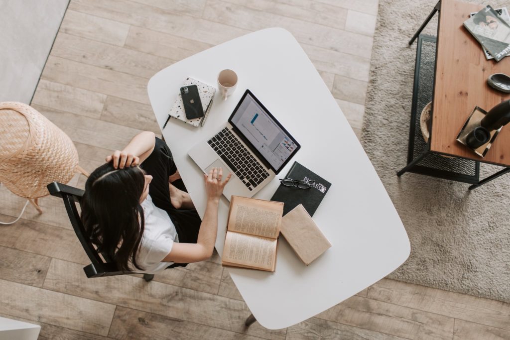 From above of young woman with long dark hair in casual clothes working at table and browsing netbook while sitting in modern workplace and touching hair