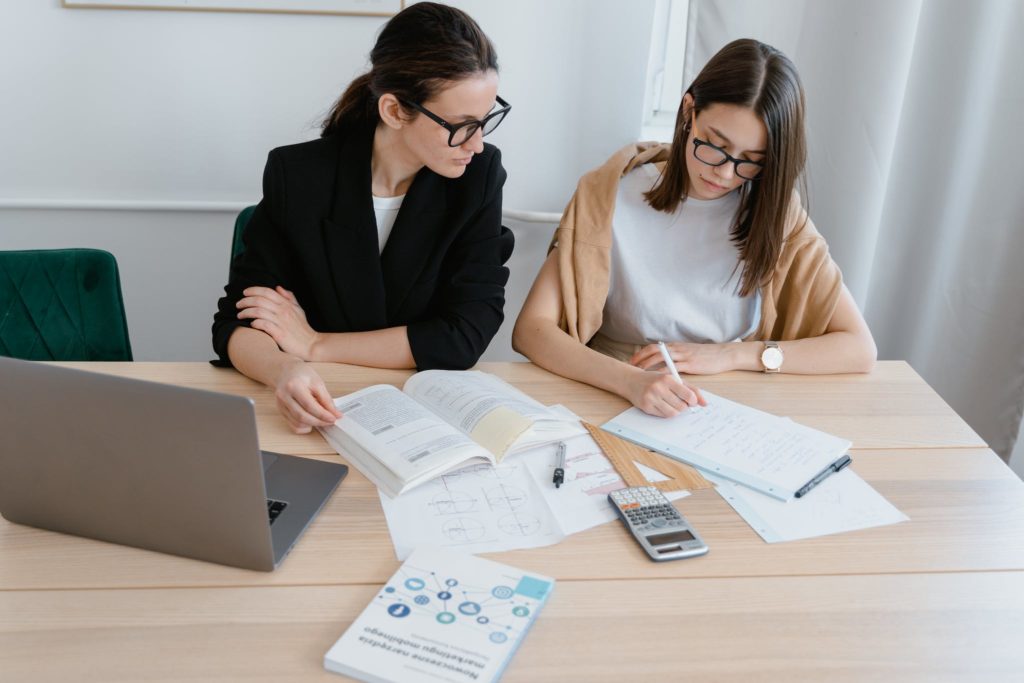 Woman in White Shirt Writing Notes Beside Her Instructor