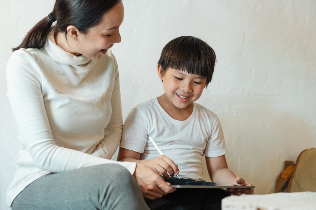 Crop happy ethnic mother sharing tablet with son at home