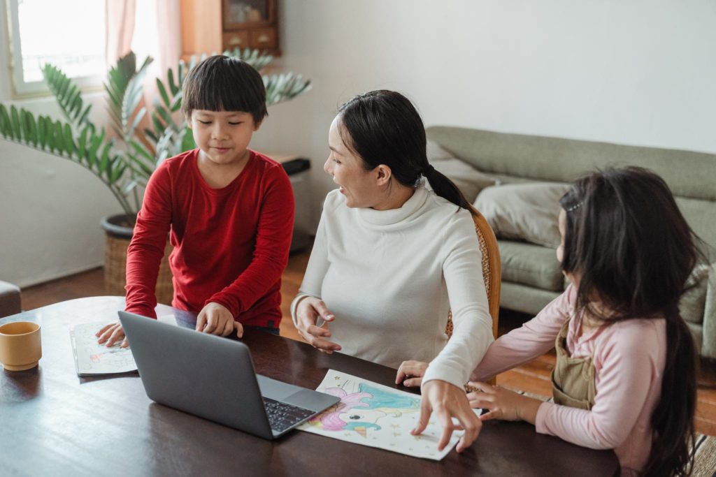 Ethnic mother sitting at table and watching paintings of little kids