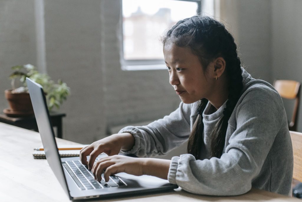 Focused Asian girl typing on laptop at home