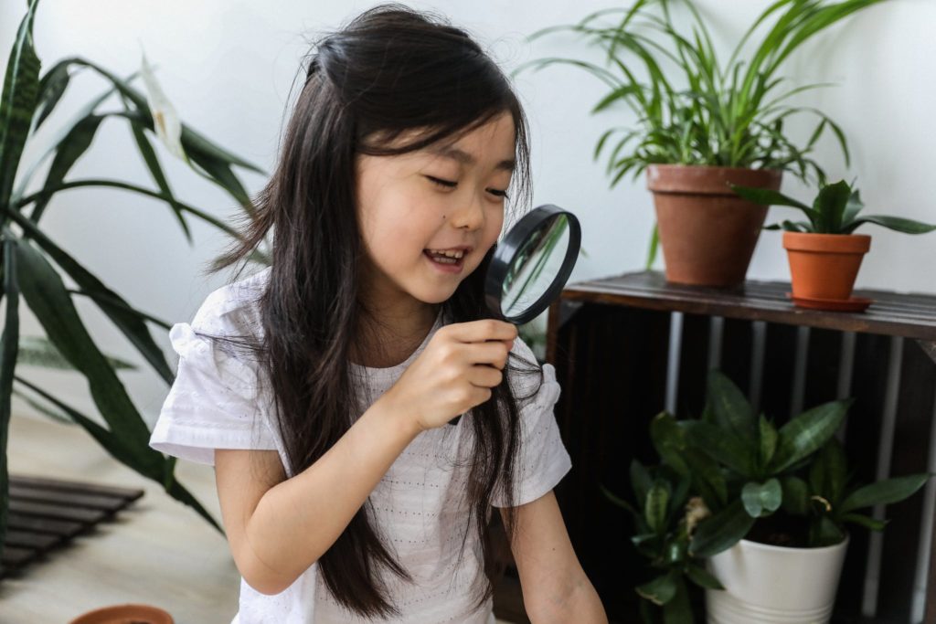 Little happy cute Asian girl looking at magnifier